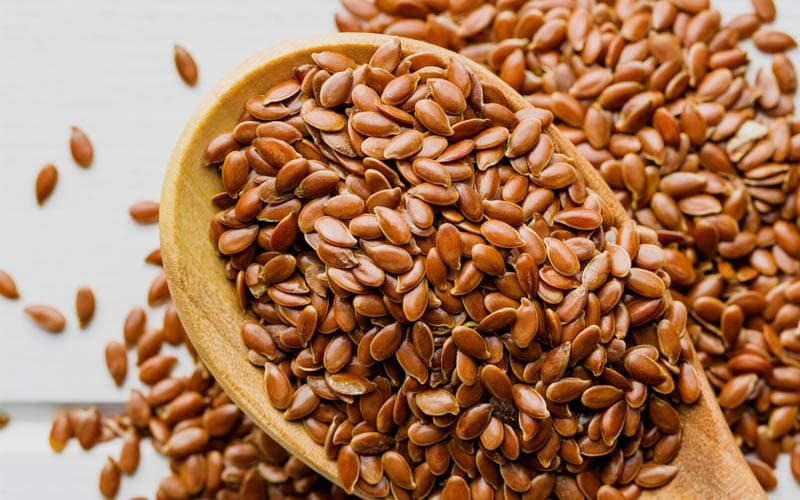 Whole brown flax seeds in a wooden spoon over a light background — a daily superfood source of omega-3, fibre and lignans
