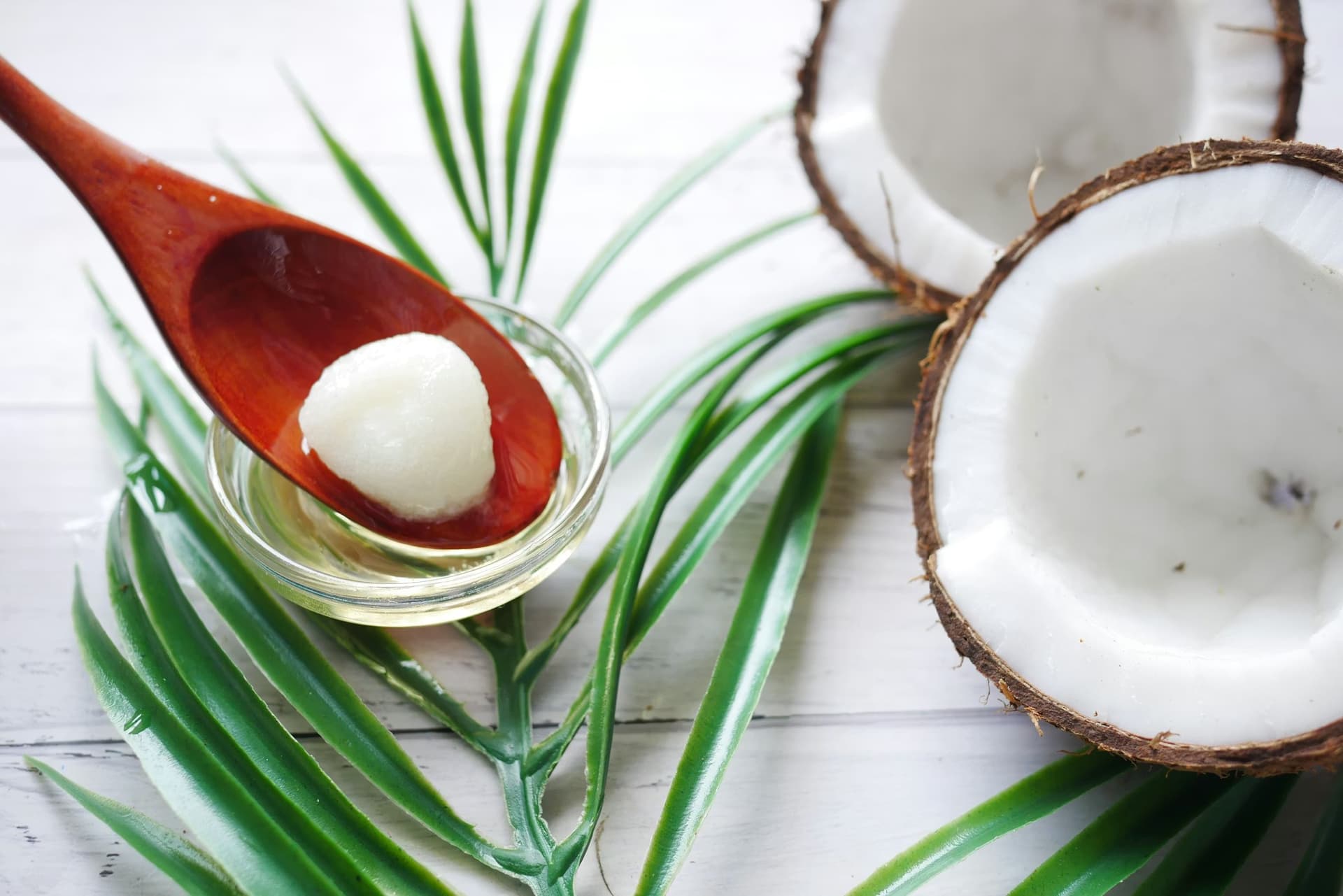 Virgin coconut oil in a glass bowl and wooden spoon beside fresh halved coconuts and palm leaves — a timeless natural superfood