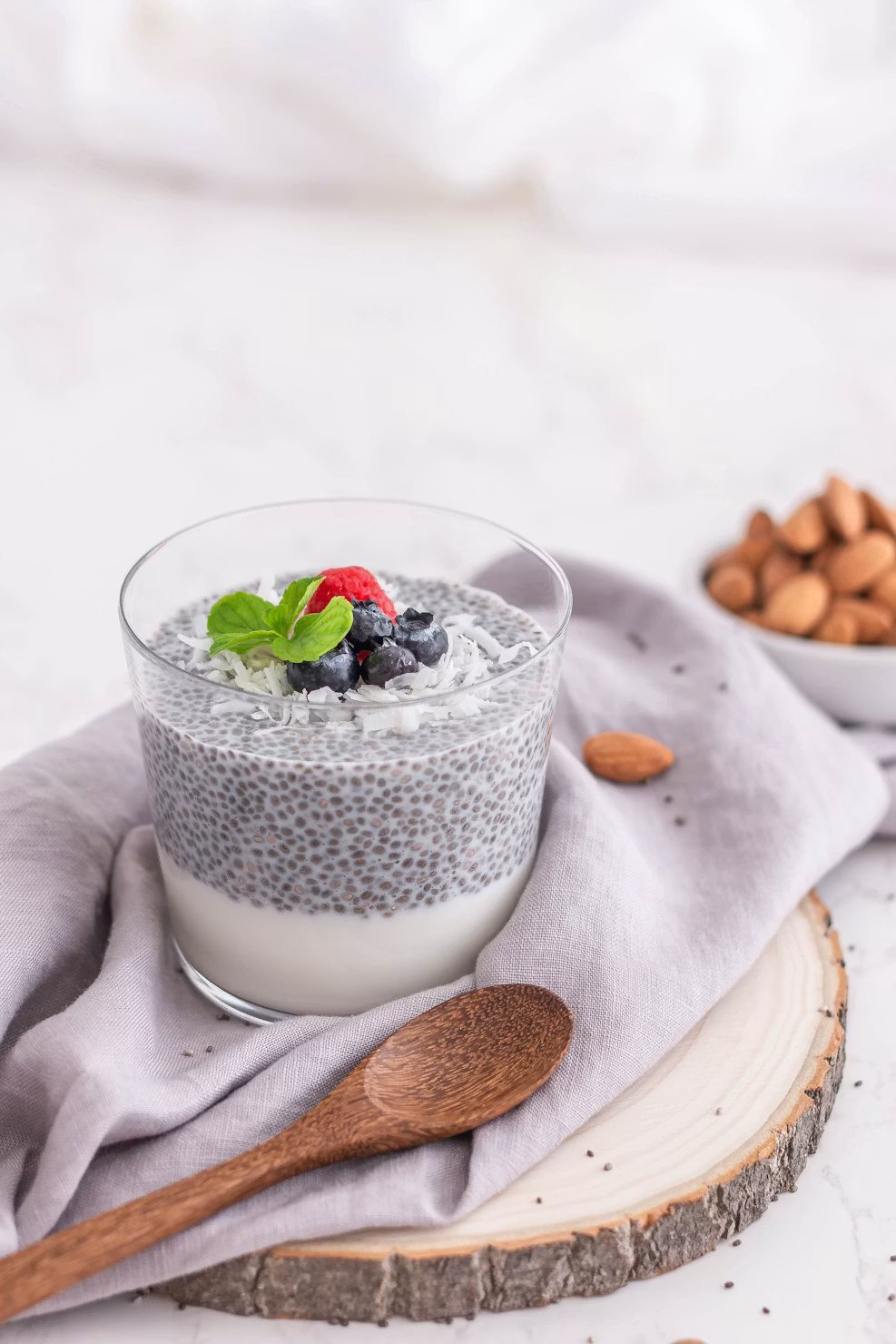 Chia pudding in a glass topped with blueberries, raspberry, coconut and mint — soaked chia forms a soft gel ideal for breakfast bowls